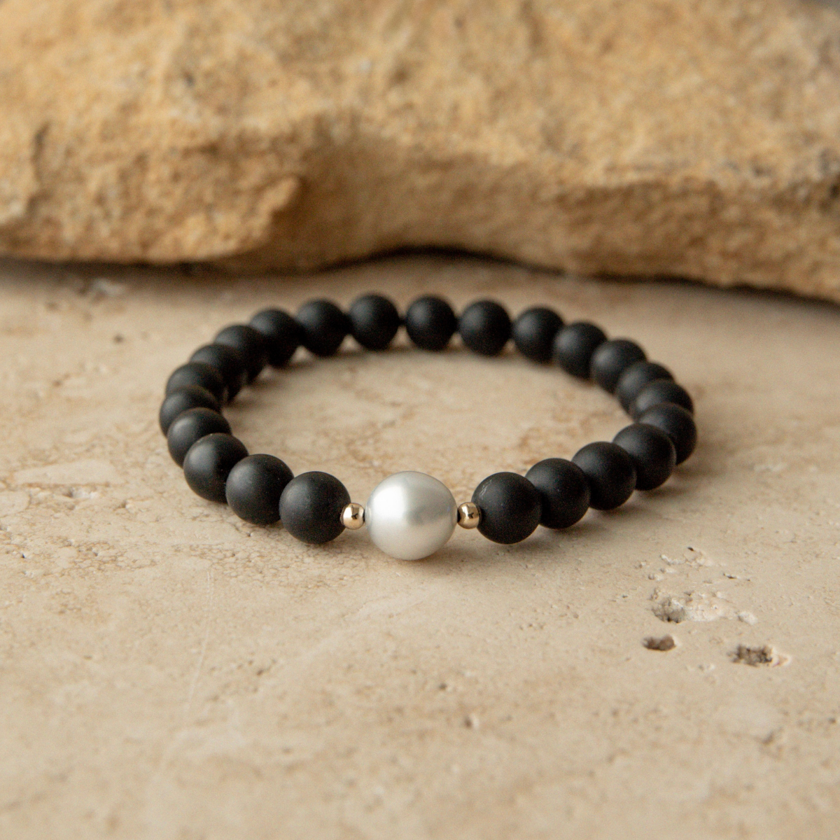 Black beaded onyx bracelet with a pearl on a beige surface