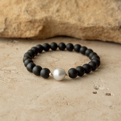 Black beaded onyx bracelet with a pearl on a beige surface
