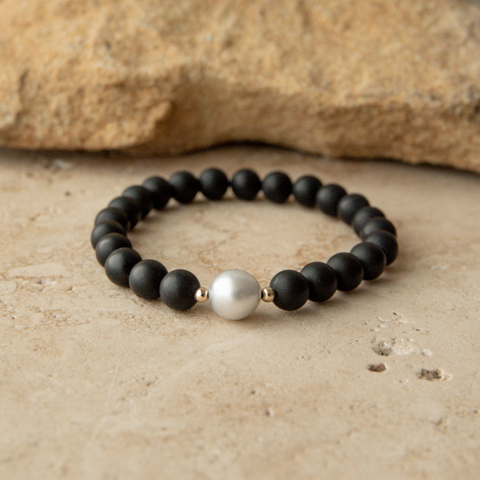 Black beaded onyx bracelet with a pearl on a beige surface