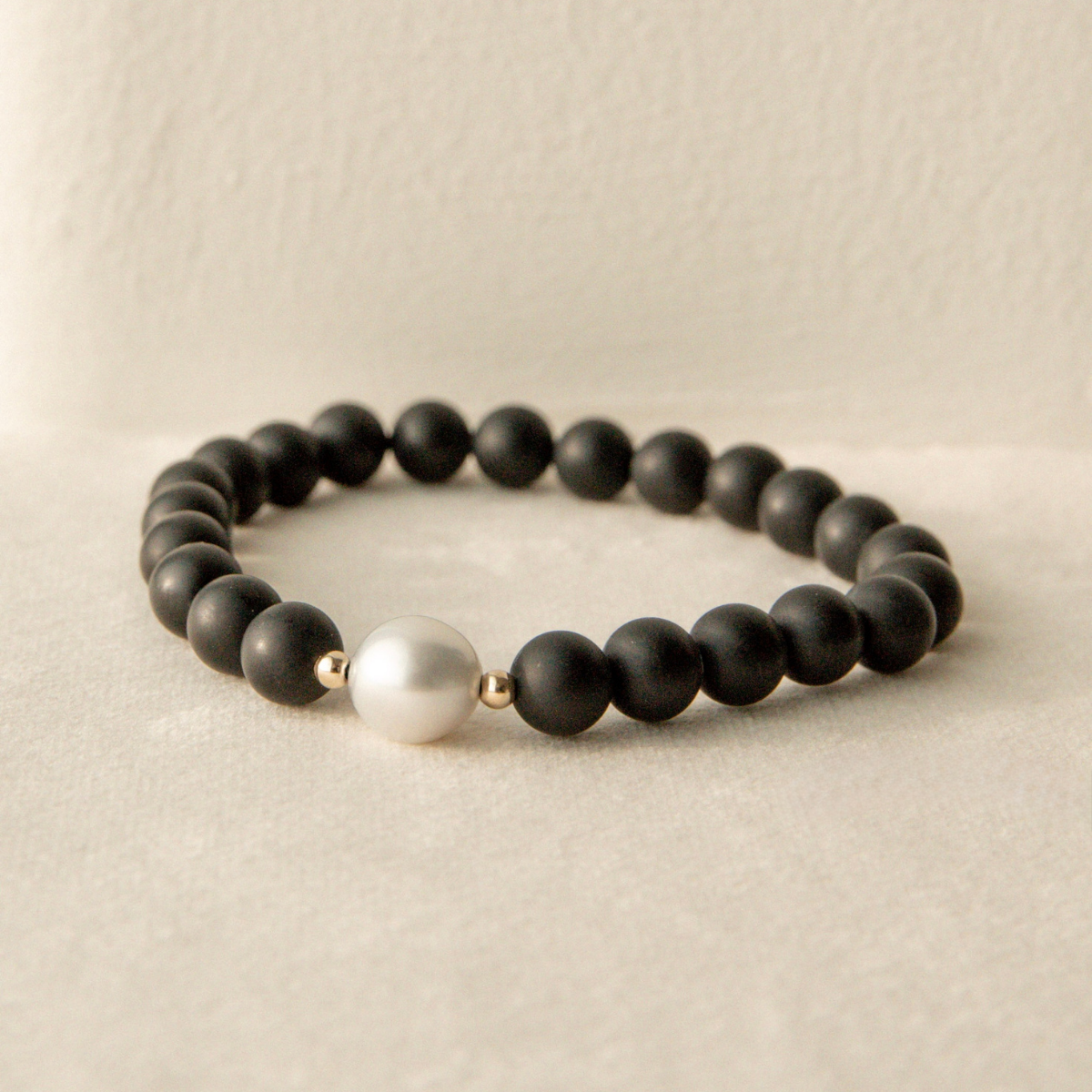 Black beaded onyx bracelet with a white pearl on a beige background