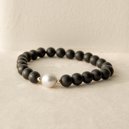 Black beaded onyx bracelet with a white pearl on a beige background