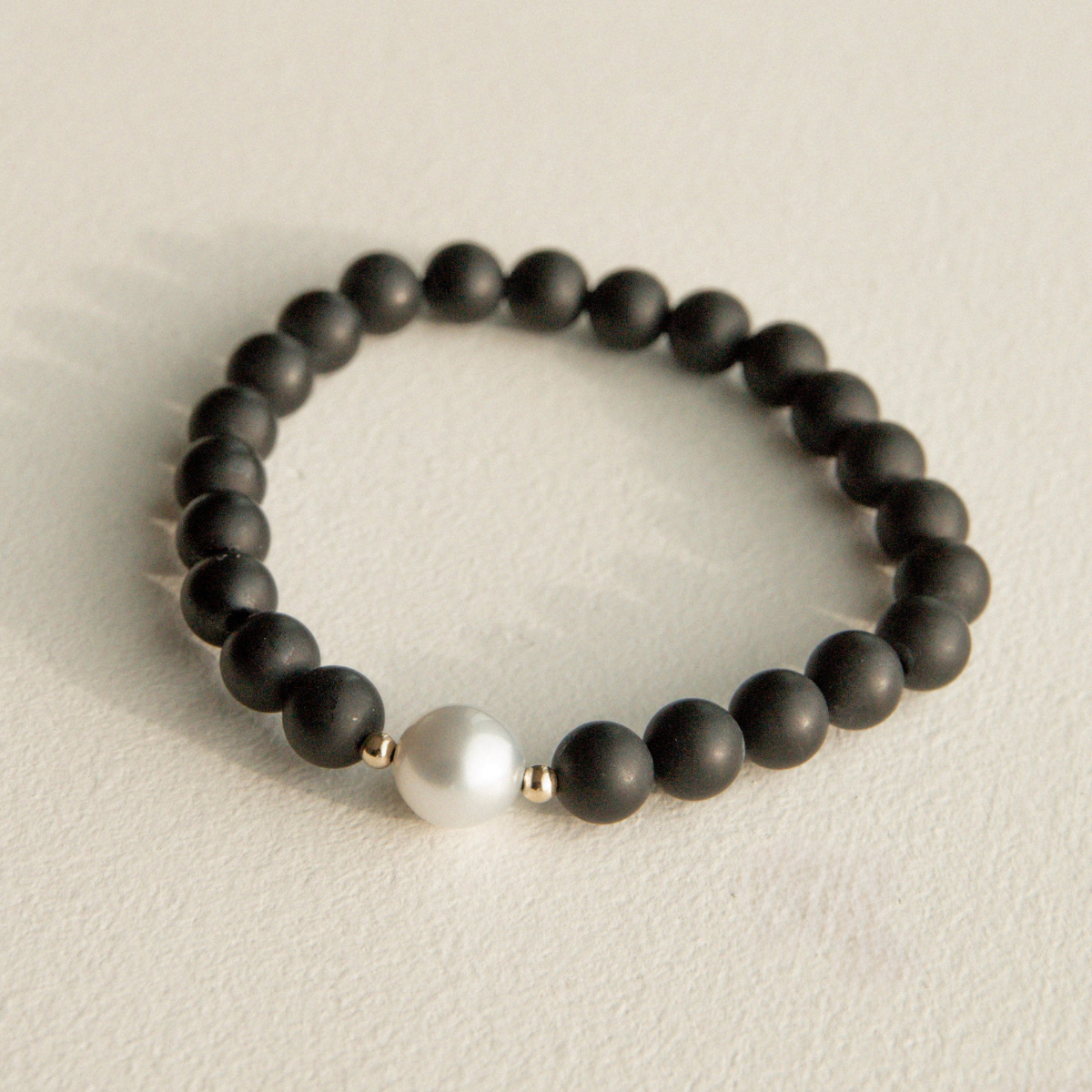Black beaded onyx bracelet with a single white pearl on a beige background