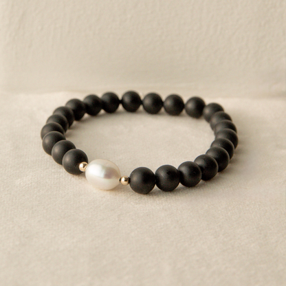 Black beaded onyx bracelet with a pearl on a beige background