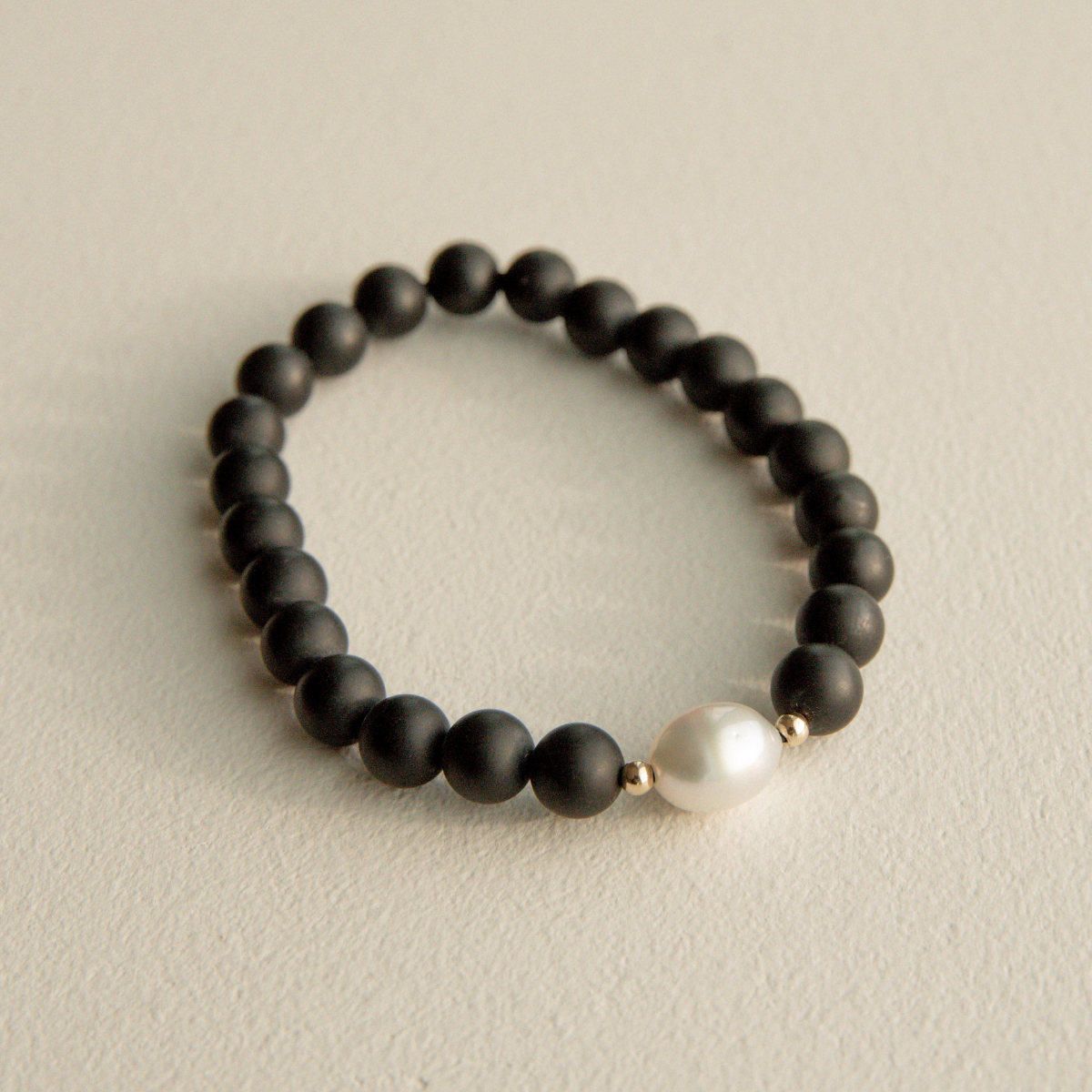 Black beaded onyx bracelet with a pearl on a beige background