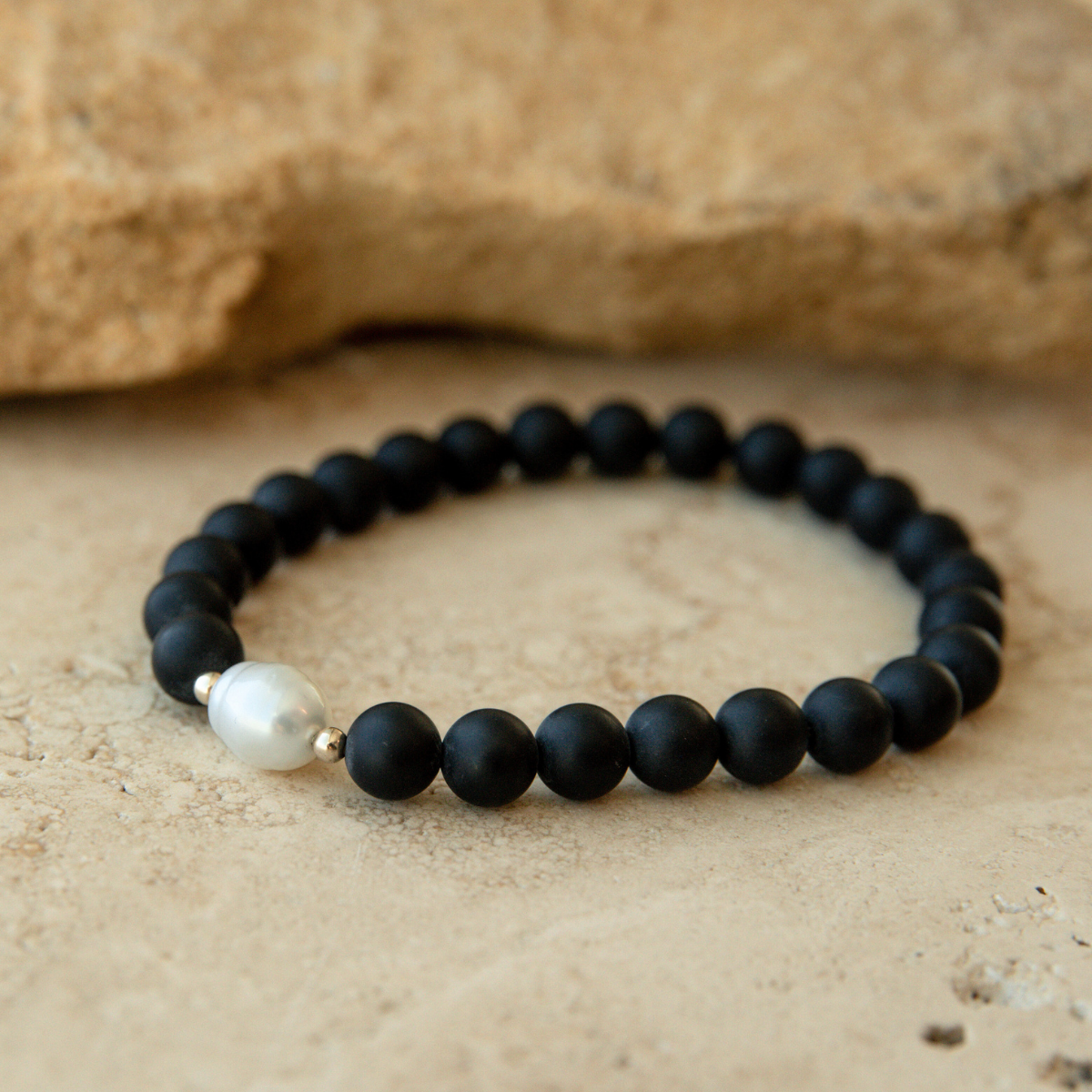 Black onyx beaded bracelet with an Australian South Sea circle pearl on a beige stone background