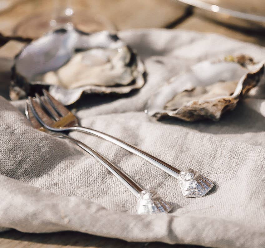 Two oysters on a bed of linen with a oyster forks beside them.
