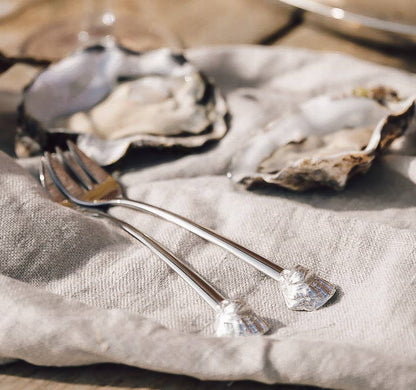 Two oysters on a bed of linen with a oyster forks beside them.