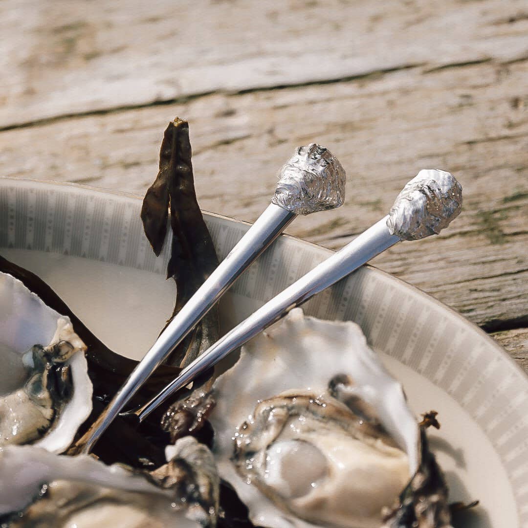 Oysters on a half shell with silver oyster shucking tools on a wooden surface