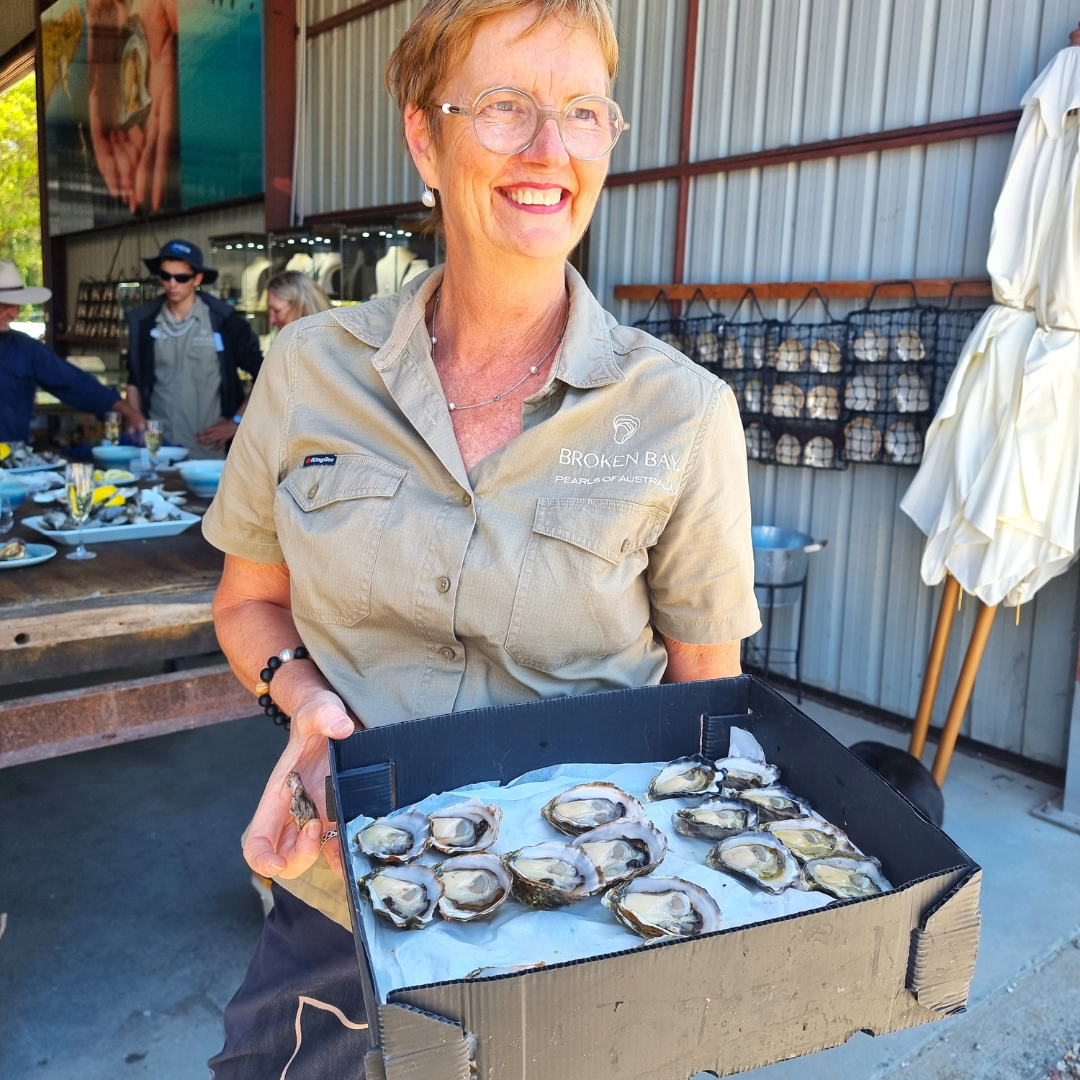 One of the friendly team members at Broken Bay Pearl Farm smiles and holds a tray of our Broken Bay grown Australian oysters, ready to be tasted during an Oyster Tasting experience at our Shellar Door.