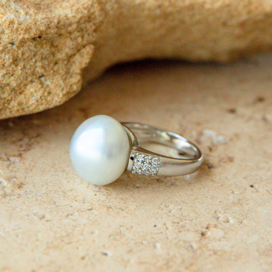 Pearl ring with diamond accents on a sandy surface