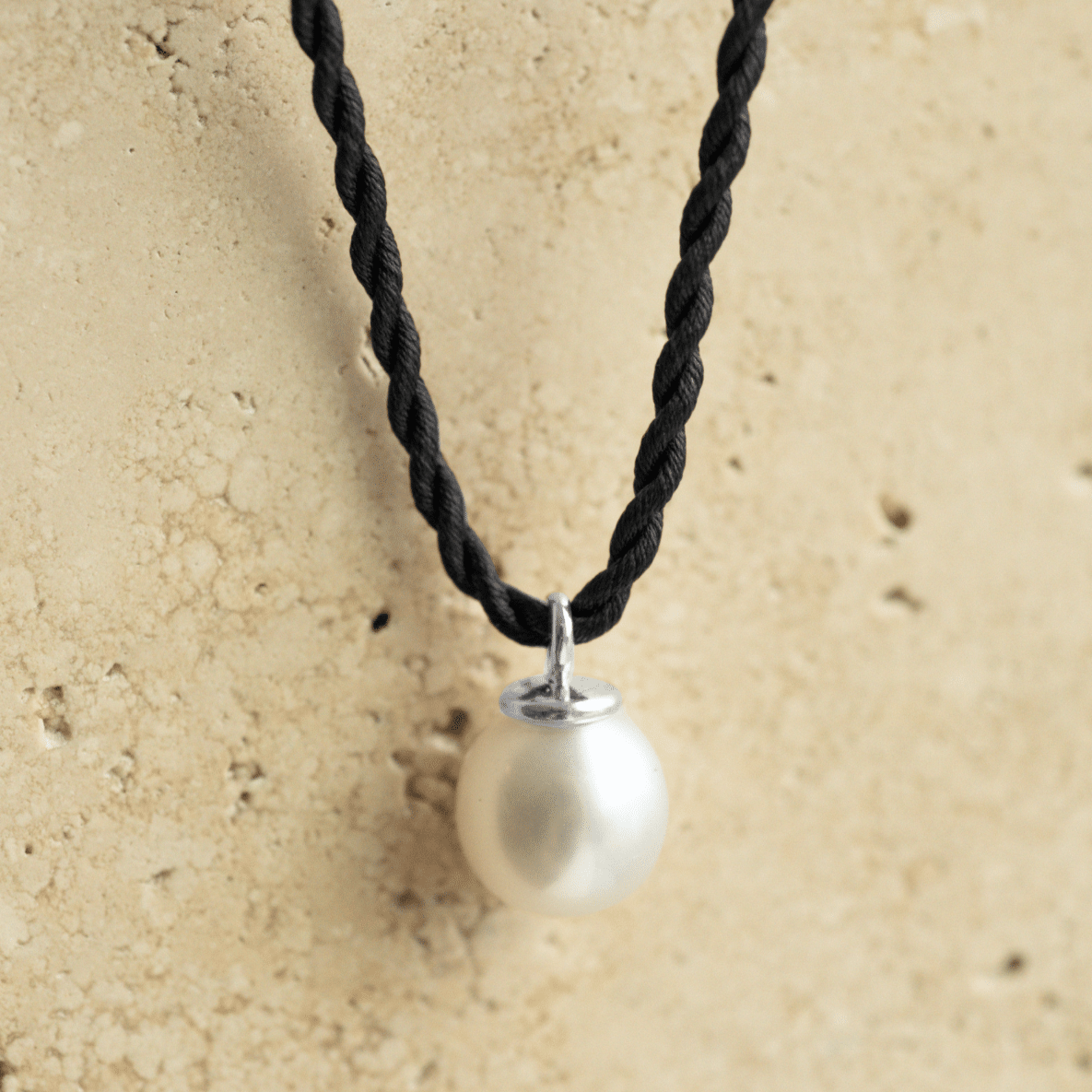 A beautiful Australian South Sea Pearl Charm set in gold sitting on a silk cord rope.