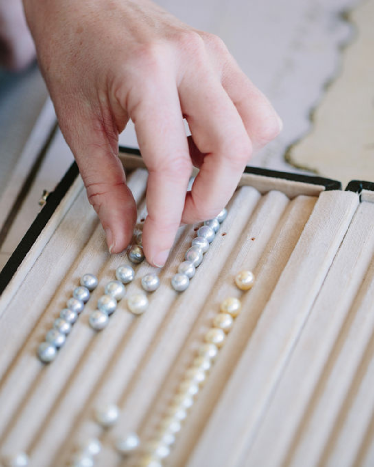 Hand sorting loose akoya pearls on a wooden tray