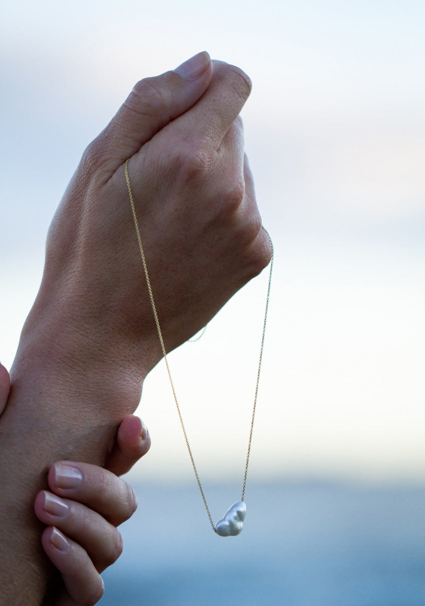 A person holds their Australian South Sea keshi pearl set on a beautiful chain necklace.