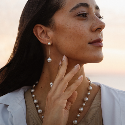 Woman wearing pearl earrings and necklace against a blurred natural background