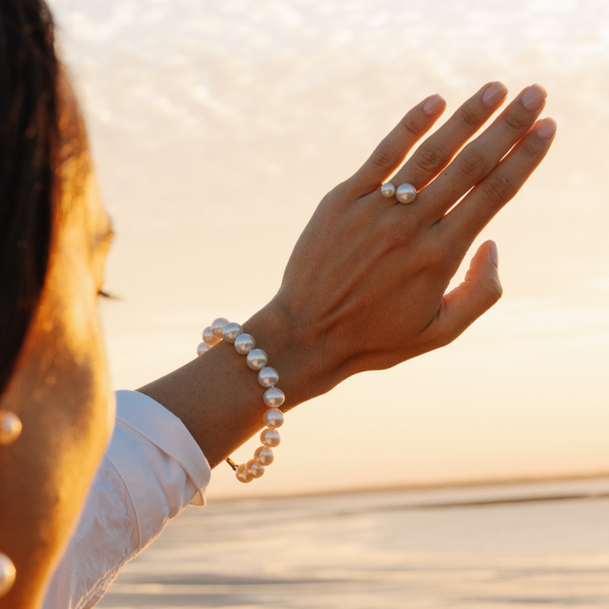 Hand with pearl bracelet and pearl ring against a sunset background