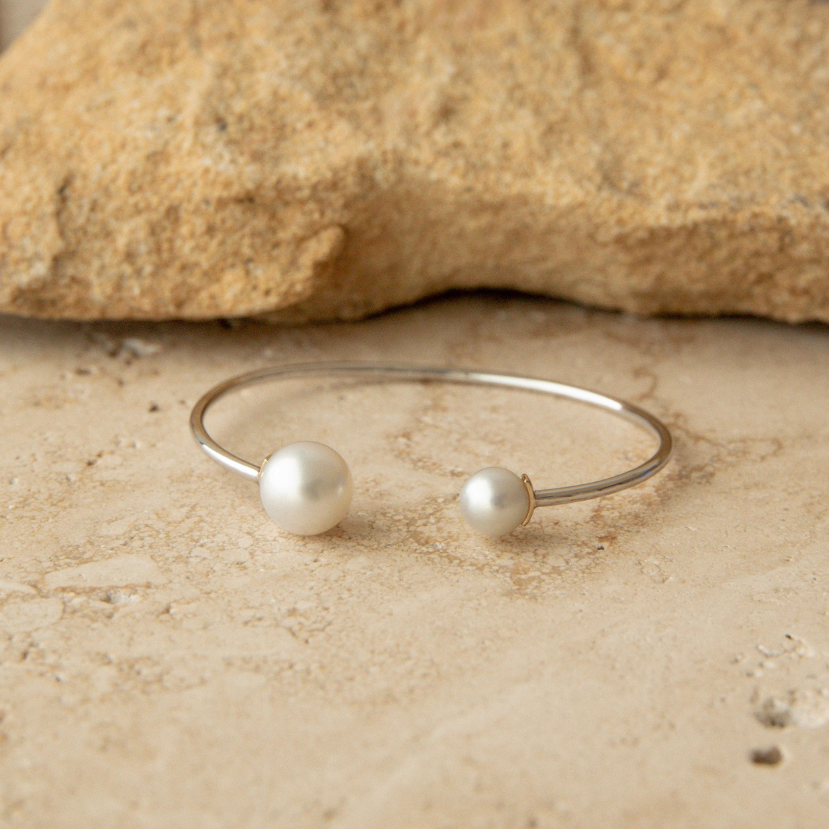A pearl bangle with two species of pearls, South Sea and Akoya, sits on a natural tile background.