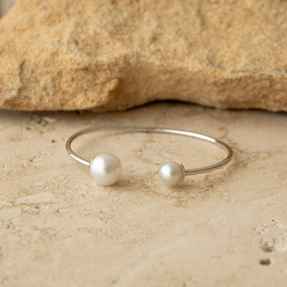 A pearl bangle with two species of pearls, South Sea and Akoya, sits on a natural tile background.