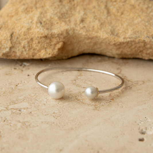 A pearl bangle with two species of pearls, South Sea and Akoya, sits on a natural tile background.