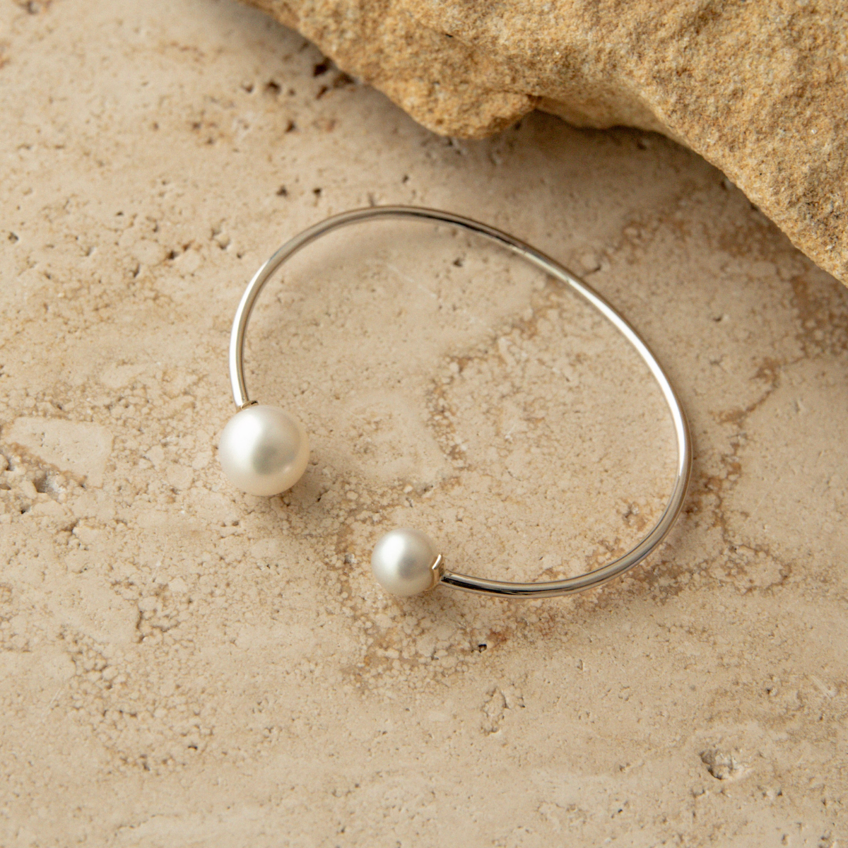 Silver bracelet with South Sea and Akoya pearls on a beige stone surface