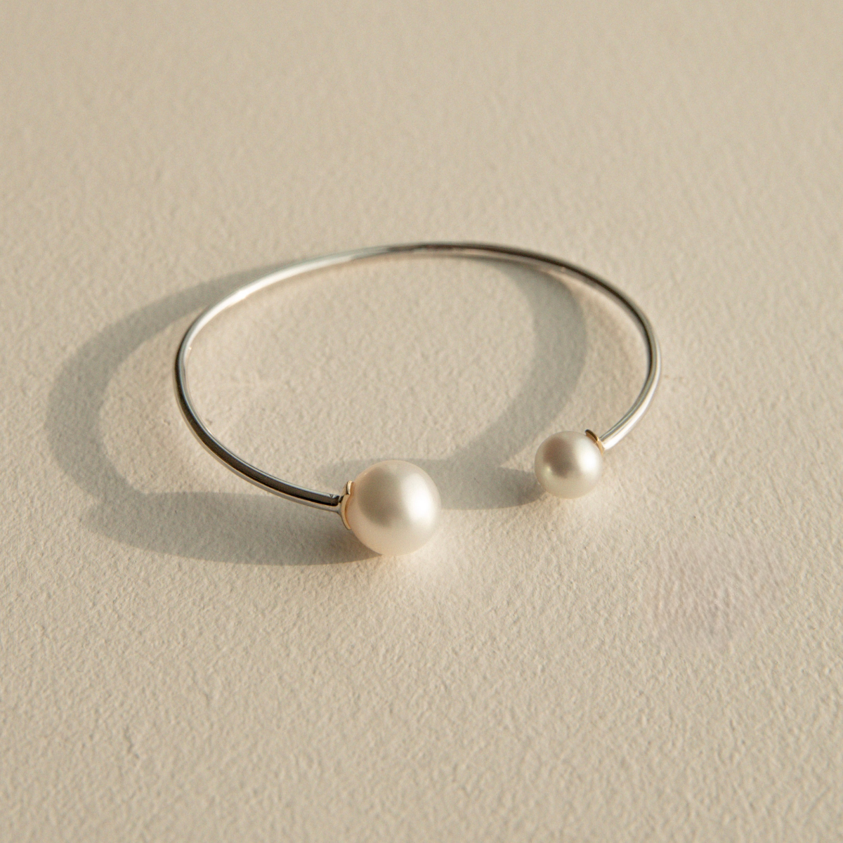 Silver bracelet with South Sea and Akoya pearls on a beige stone surface