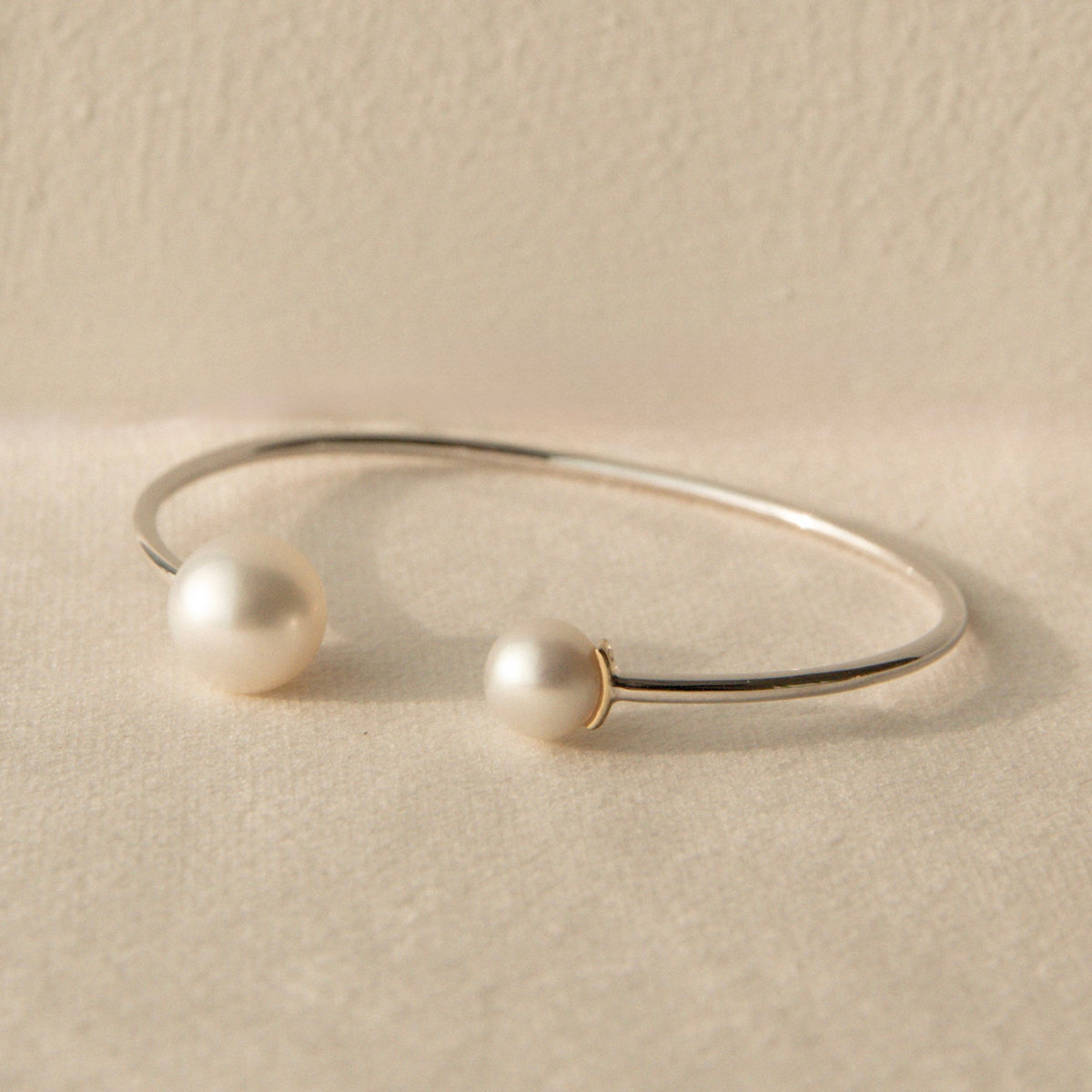 Silver bracelet with South Sea and Akoya pearls on a beige stone surface