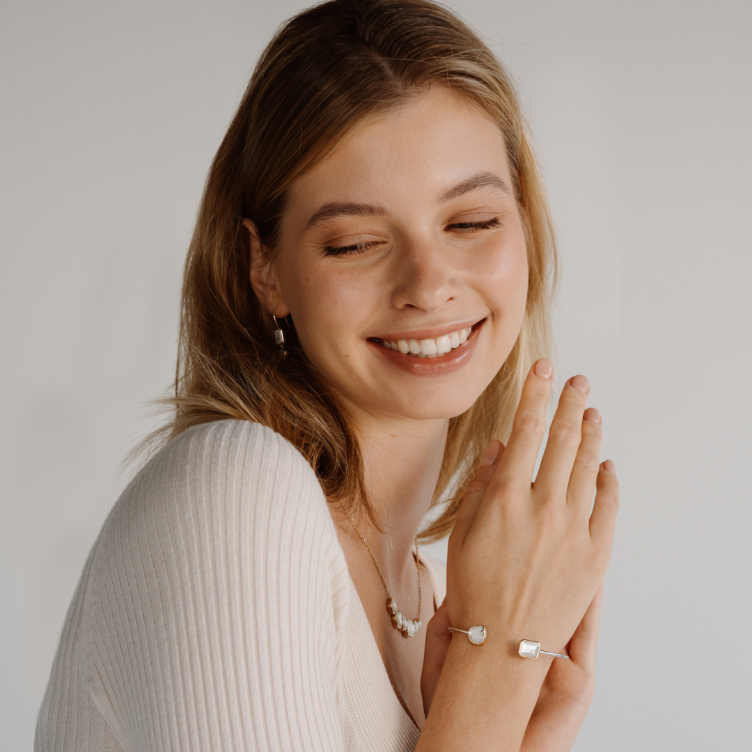 A woman smiles while wearing her Radiance Emerald & Pear Cut Bangle features faceted Mother of Pearl grown at our Cygnet Bay Pearl Farm (WA).