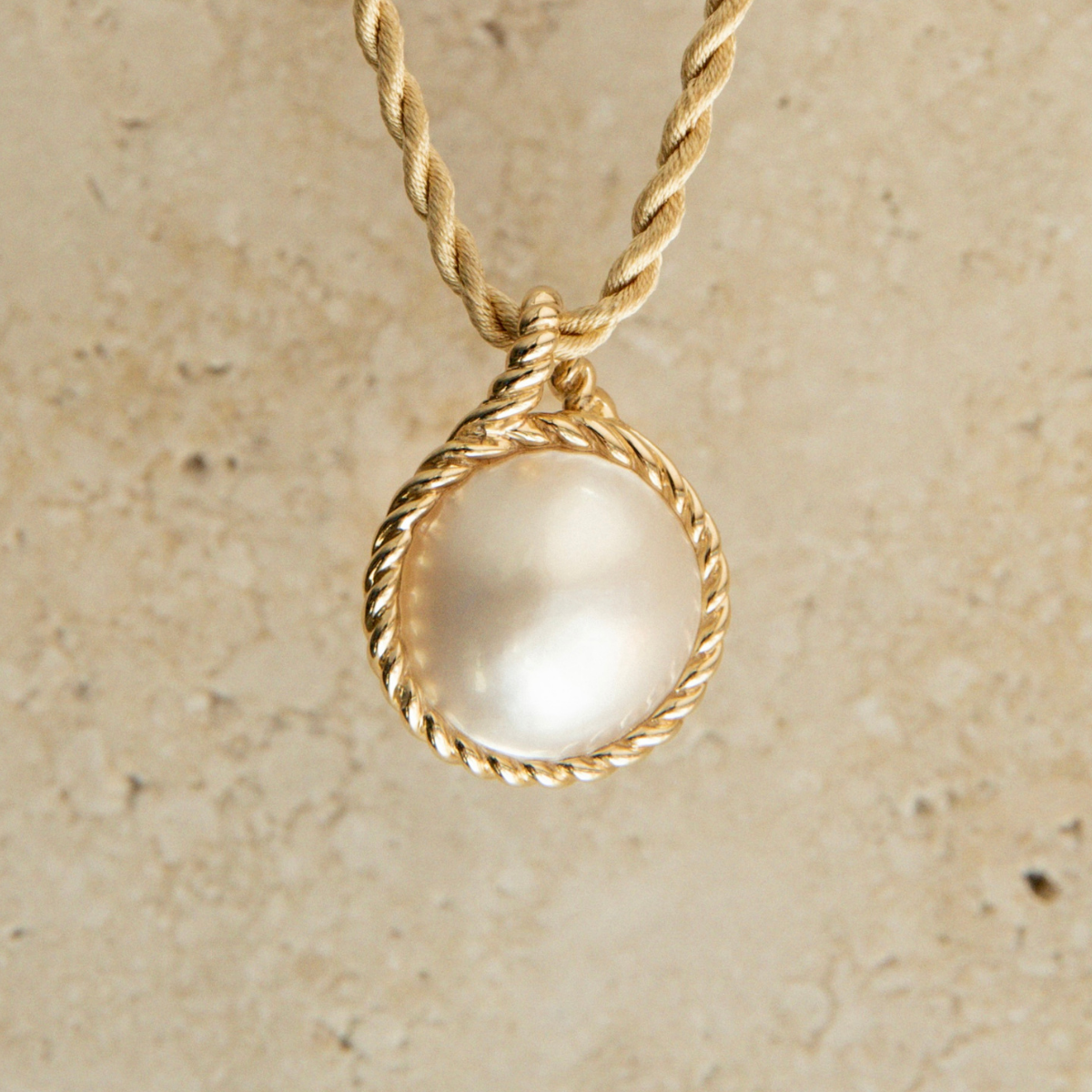 Gold necklace with a round Mabe pearl pendant on a beige background
