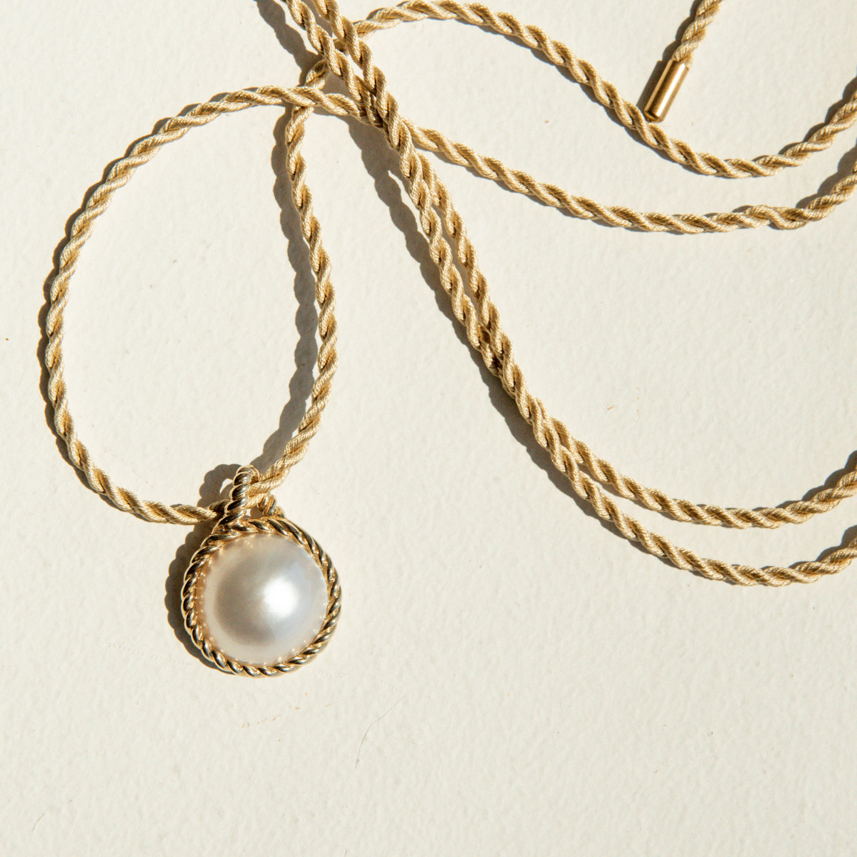 Gold necklace with a Mabe pearl pendant on a beige background