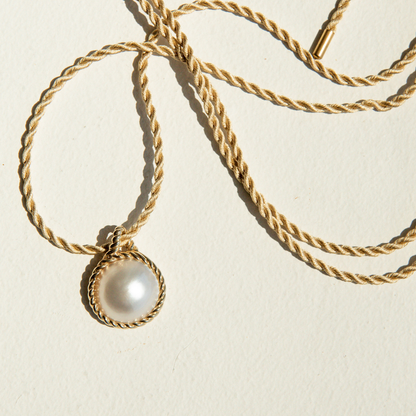 Gold necklace with a Mabe pearl pendant on a beige background
