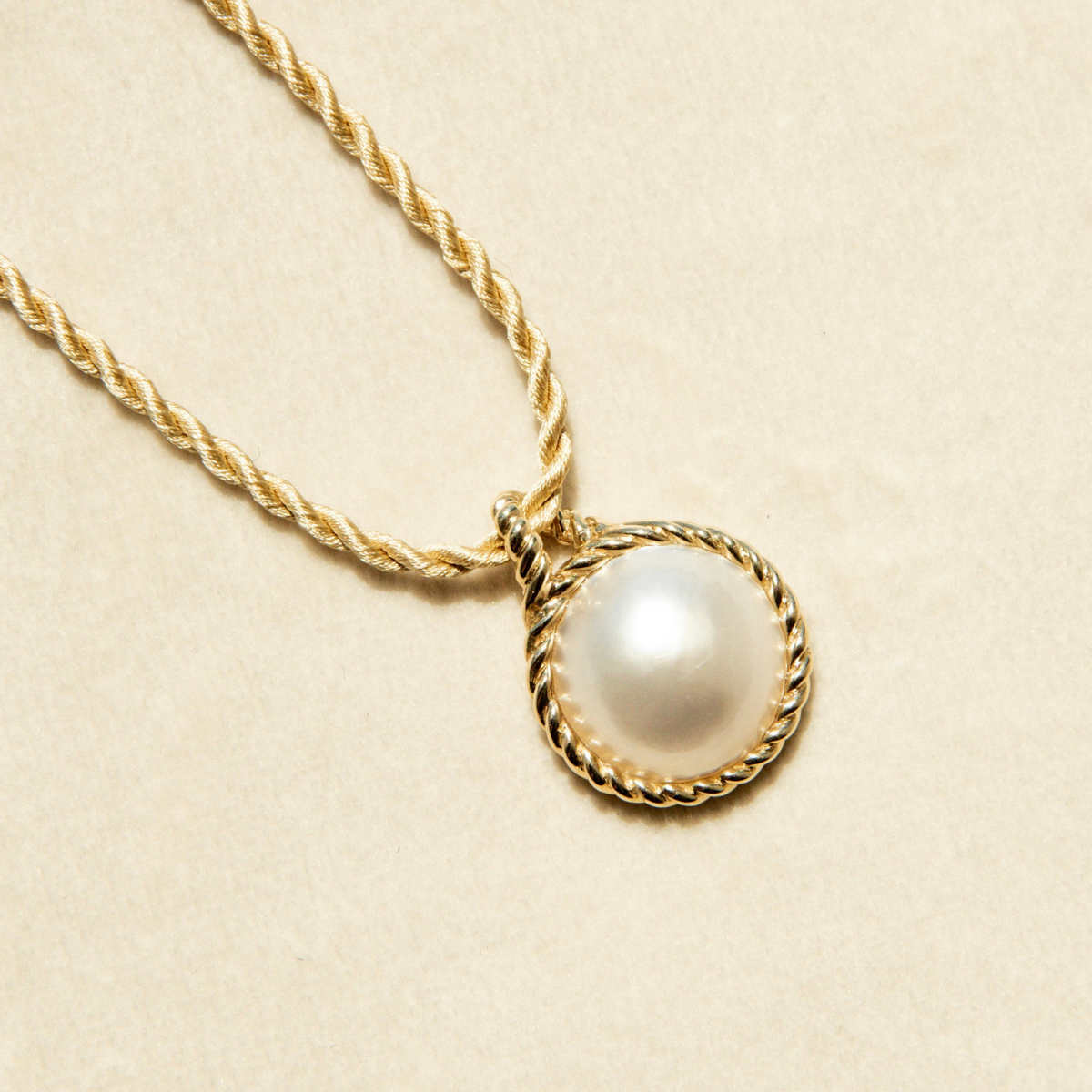 Gold necklace with a Mabe or blister pearl pendant on a beige background