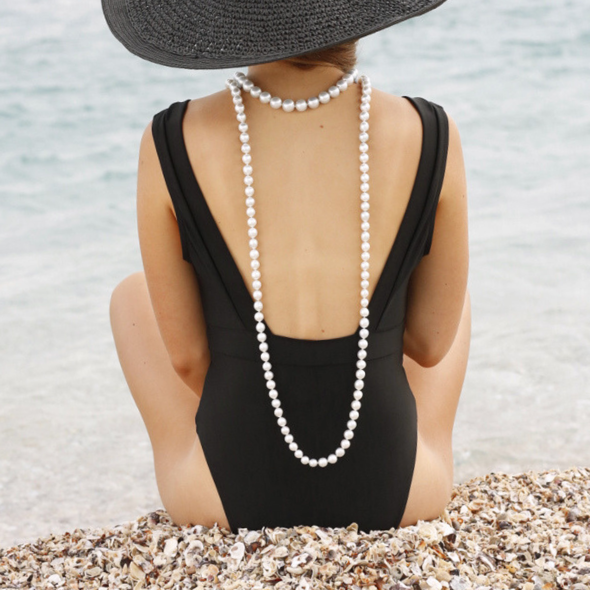 Person wearing a black swimsuit and pearl necklace on a beach.