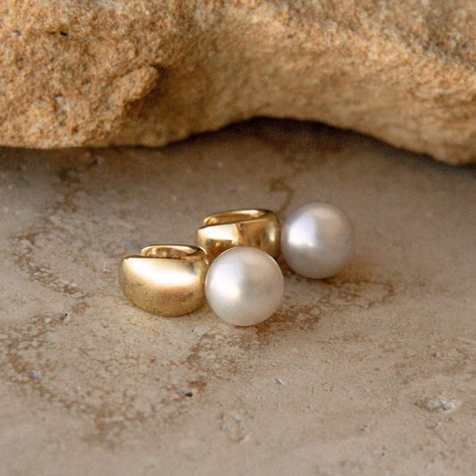 Australian South Sea pearl huggies in gold vermeil arranged on a textured stone surface with a larger rock in the background.