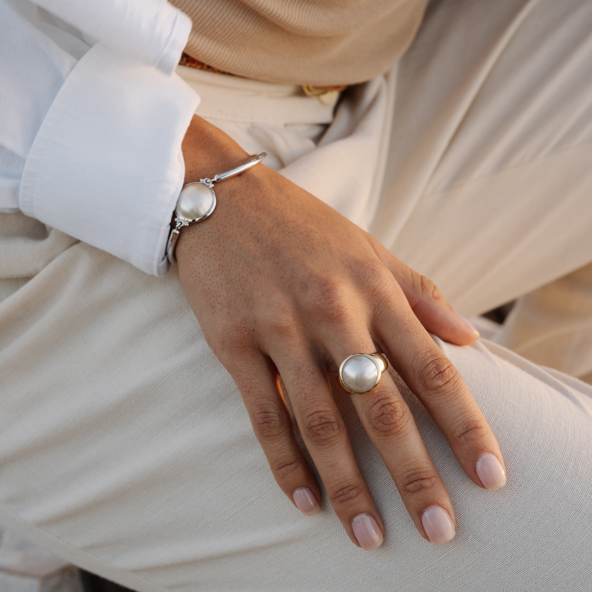Hand wearing a mabe pearl ring and mabe pearl bracelet on a neutral background