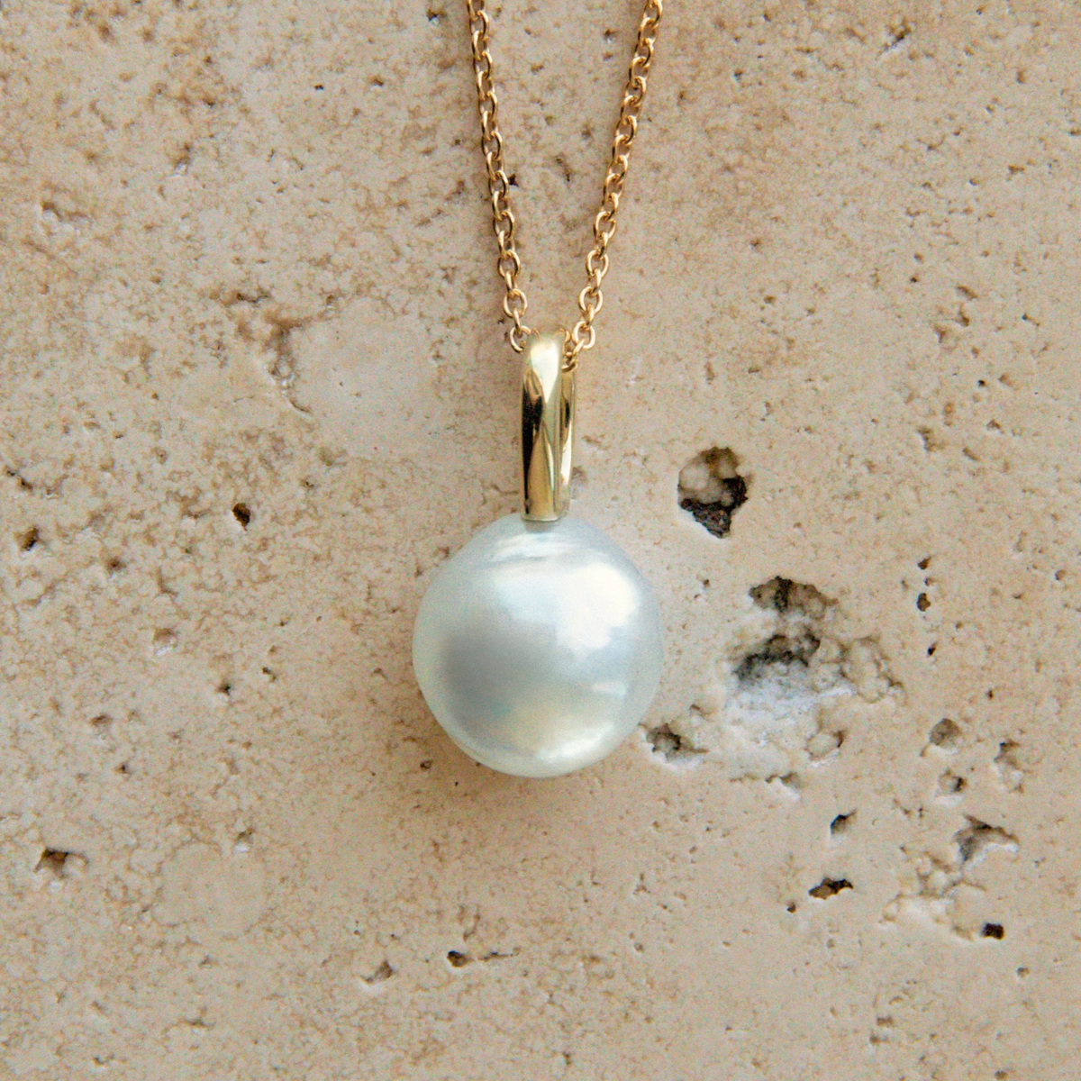 Pearl necklace with gold chain on a textured beige background