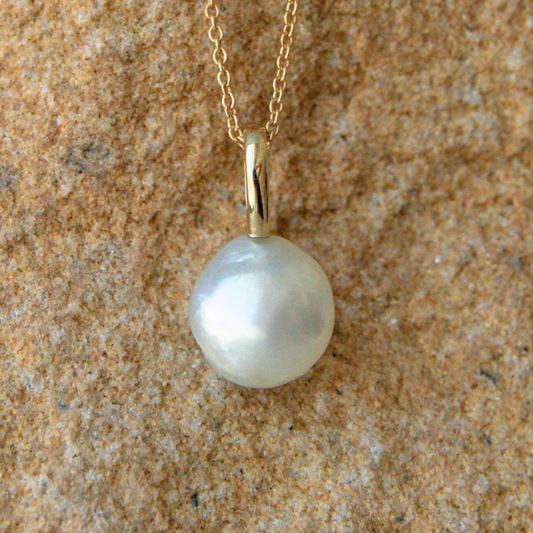 Pearl pendant on a gold chain against a textured beige background