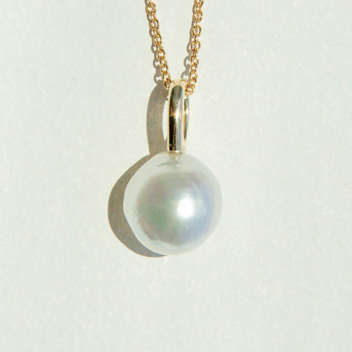 Pearl pendant on a gold chain against a light gray background