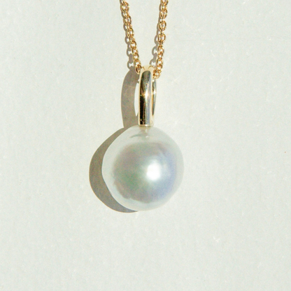 Pearl pendant on a gold chain against a light gray background