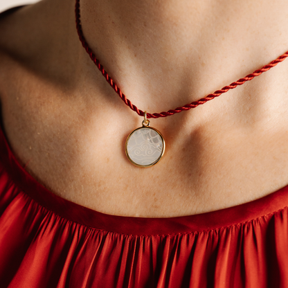 Necklace with a round pendant worn by a person in a red garment
