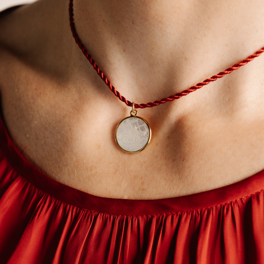 Necklace with a round pendant worn by a person in a red garment