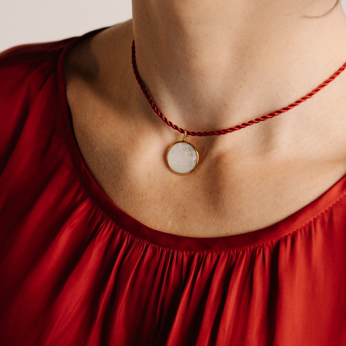 Necklace with a round pendant worn by a person in a red top against a neutral background
