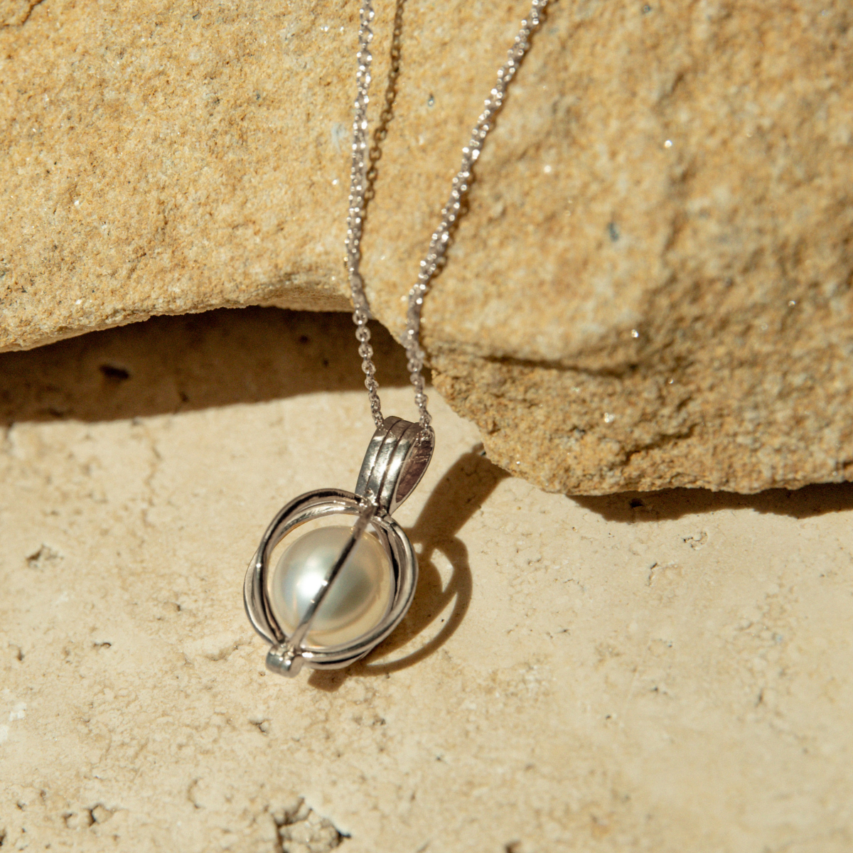 Silver necklace with a pearl cage pendant on a beige stone background