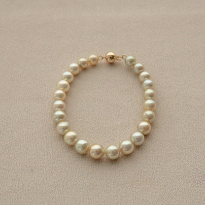 A strand of round Australian Akoya pearls set with 18ct gold, displayed on a textured beige surface.
