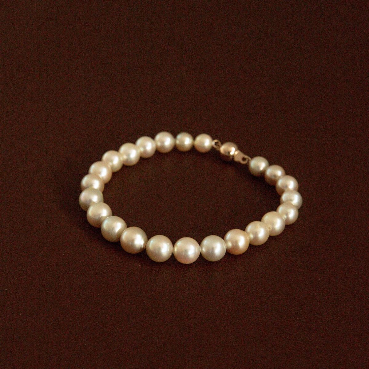 A classic strand of cream toned Australian Akoyapearls arranged in a circle, featuring an 18ct yellow gold clasp, displayed on a dark brown background.