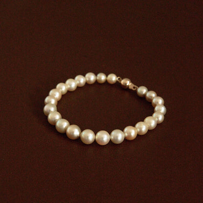 A classic strand of cream toned Australian Akoyapearls arranged in a circle, featuring an 18ct yellow gold clasp, displayed on a dark brown background.