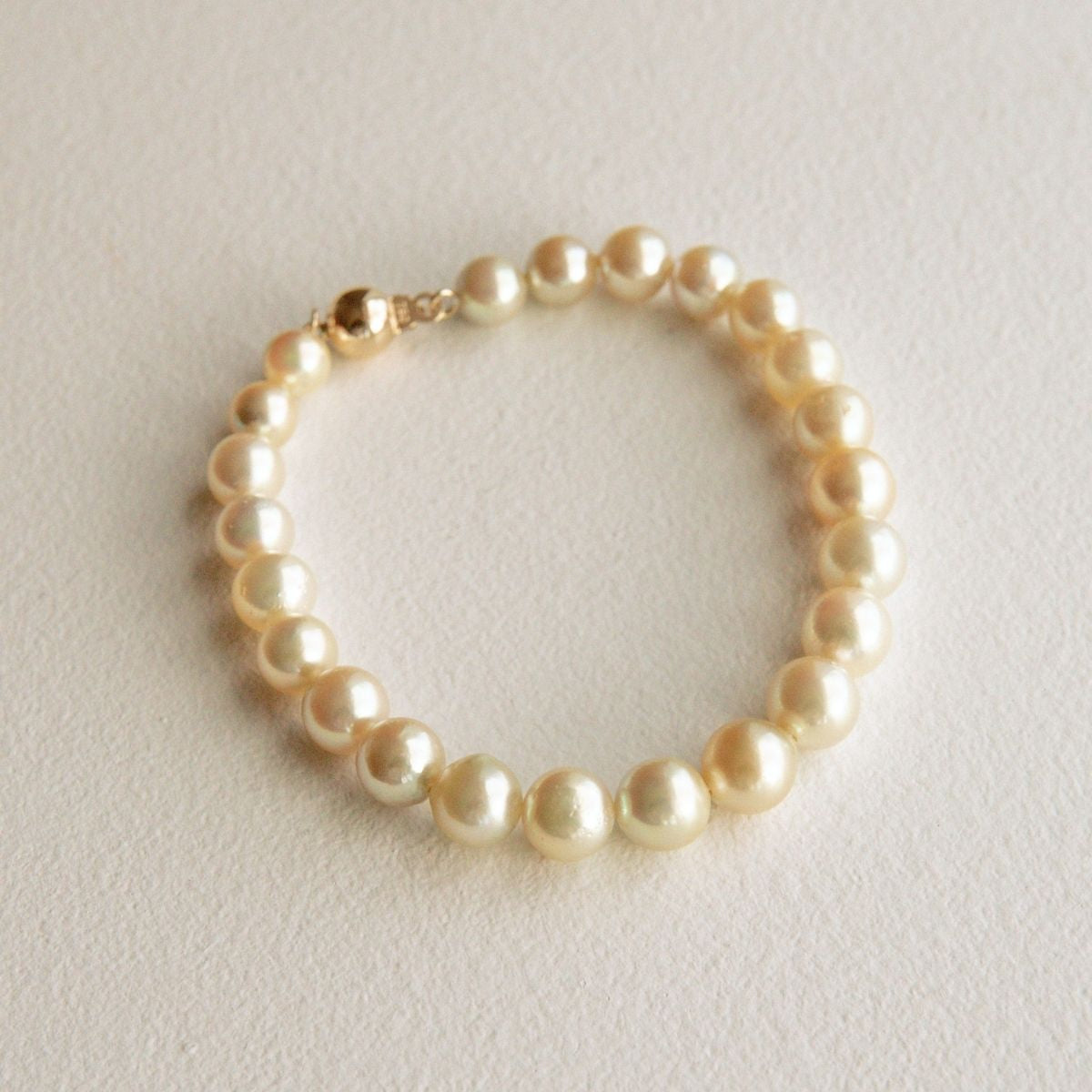 A single-strand Australian Akoya pearl bracelet with an 18ct gold clasp, displayed on a textured off-white surface.