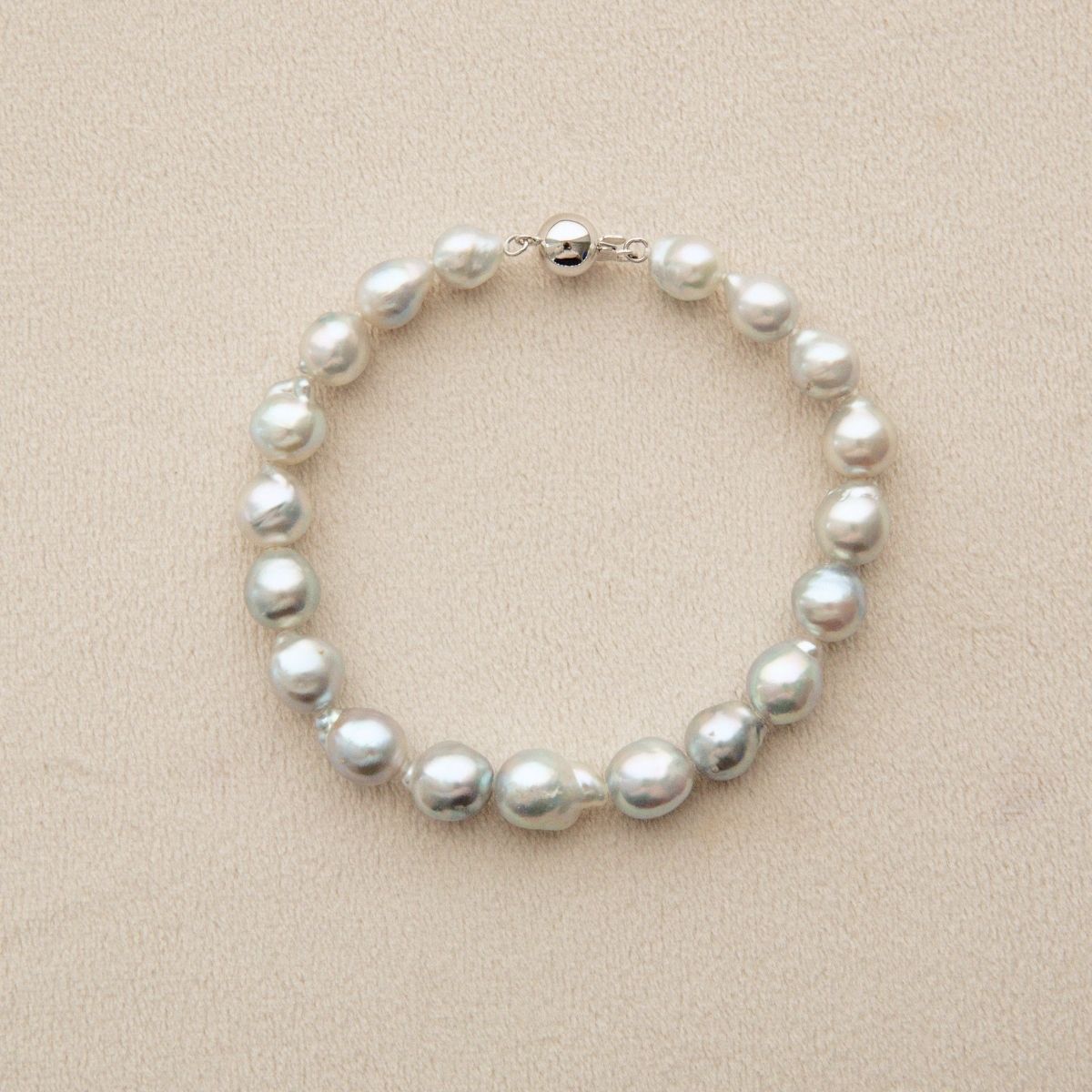 An Australian Akoya pearl strand bracelet made of irregular white pearls with an 18ct white gold clasp, displayed on a textured beige background.