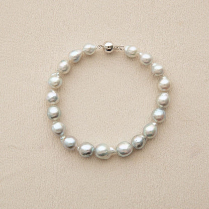 An Australian Akoya pearl strand bracelet made of irregular white pearls with an 18ct white gold clasp, displayed on a textured beige background.