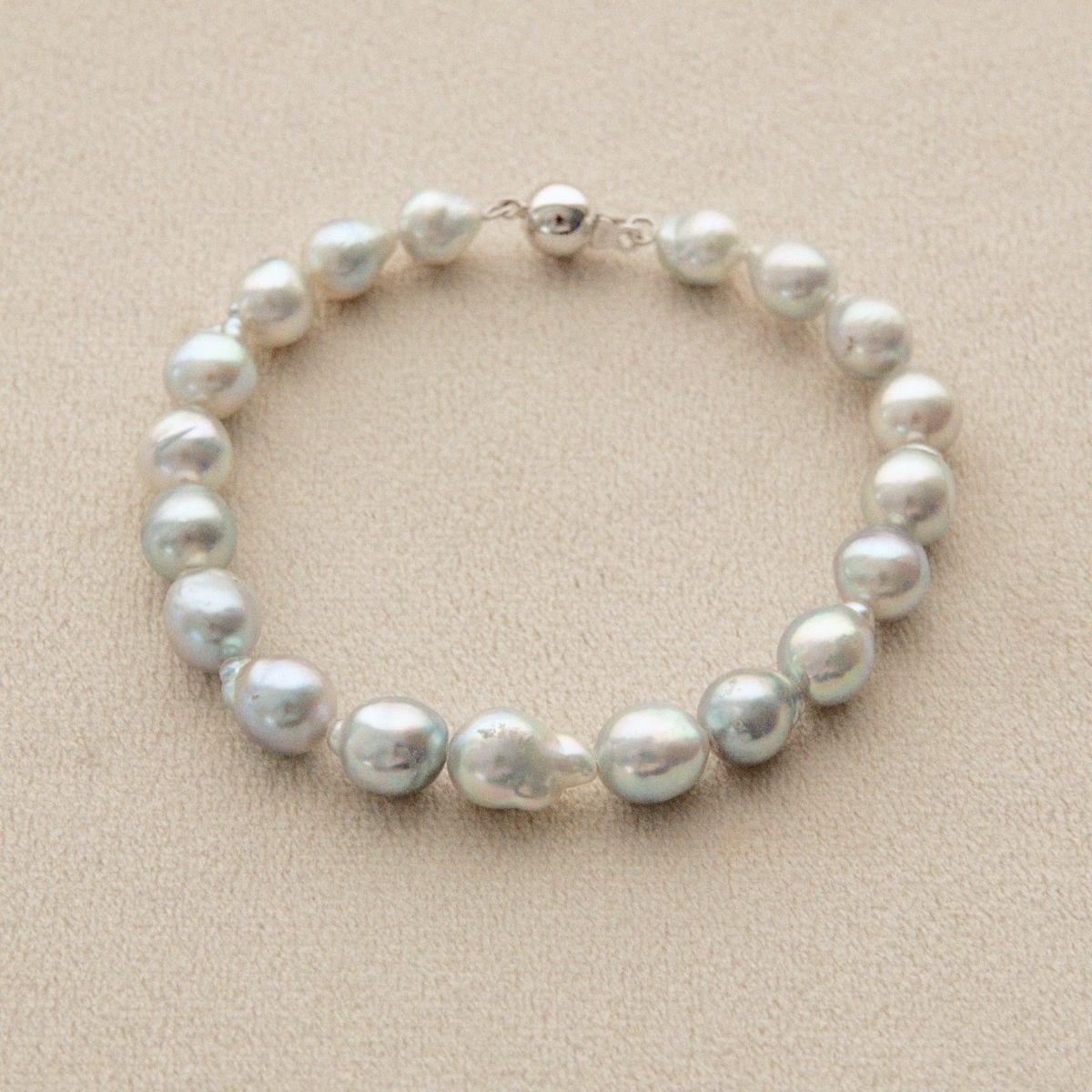 A strand bracelet made of irregular, lustrous Australian Akoya pearls with an 18ct white gold clasp, displayed on a textured beige background.