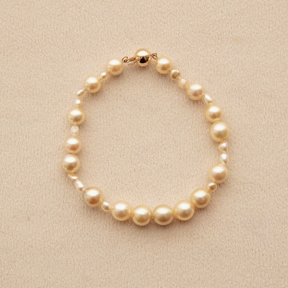 An Australian South Sea pearl strand bracelet made of golden Keshi and Akoya pearls of varying sizes, accented with a gold clasp, displayed on a textured beige background.