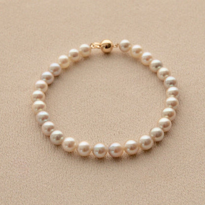 A single-strand pearl bracelet with a gold clasp, displayed on a textured beige surface.